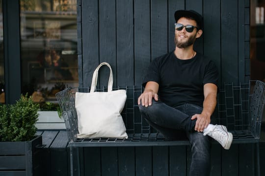 ベンチに座るサングラスをかけた男性と横に置かれるリネンのトートバッグ